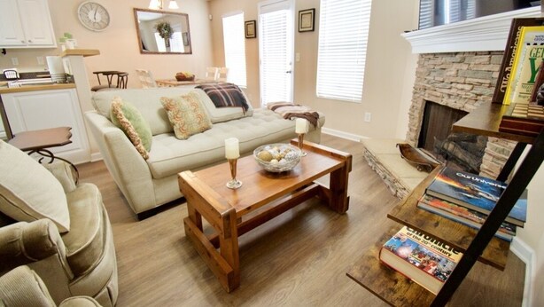 A cozy living room with a sofa, coffee table, and fireplace. There are books on the fireplace mantel and a clock on the wall. - Charming, Stylish and Cozy 3 Bedroom Townhouse near Athens (Winder)