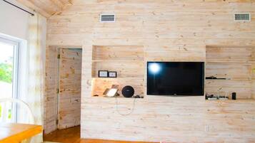 Een kamer met houten lambrisering, een flatscreen televisie aan de muur, een klein plankje met decoratieve objecten en een raam dat voor daglicht zorgt.