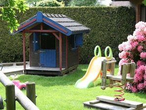 Ein Kinderspielbereich mit Rutsche, einem kleinen Holzspielhaus und einer Schaukel.