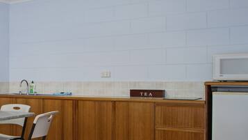 A compact kitchen with a microwave, a sink, and a tea sign on the counter.