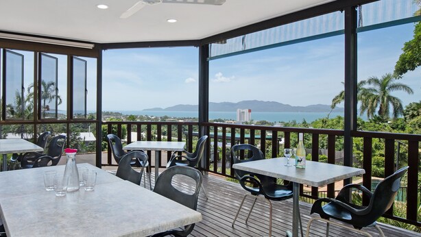 A balcony with tables and chairs, overlooking a scenic view of the sea and mountains. - Island View Motel (North Ward)
