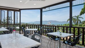 A balcony with tables and chairs, overlooking a scenic view of the sea and mountains. - Island View Motel (North Ward)