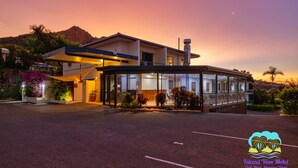 A modern motel with a glass facade, a covered entrance, and a mountain backdrop. - Island View Motel (North Ward)