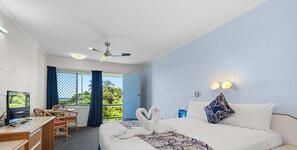 A hotel room with a bed, a desk with a computer, a chair, a ceiling fan, and a view of the outdoors. - Island View Motel (North Ward)
