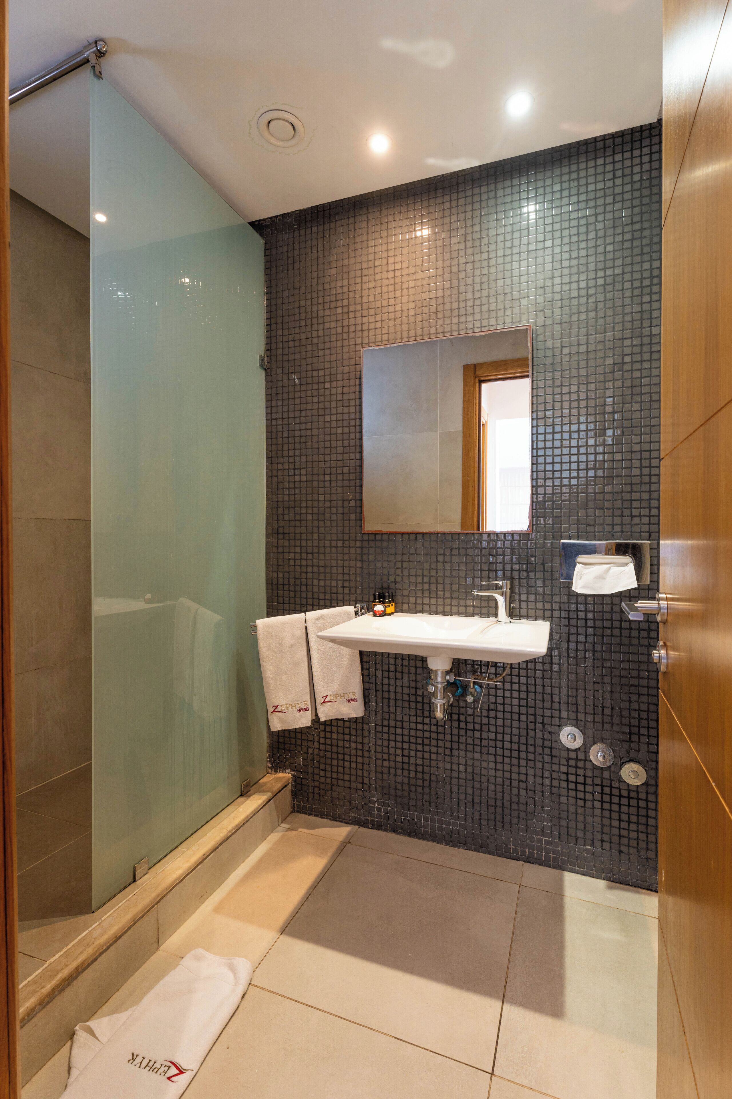 Une salle de bain avec une douche à parois de verre, un lavabo blanc et un mur recouvert de carreaux.