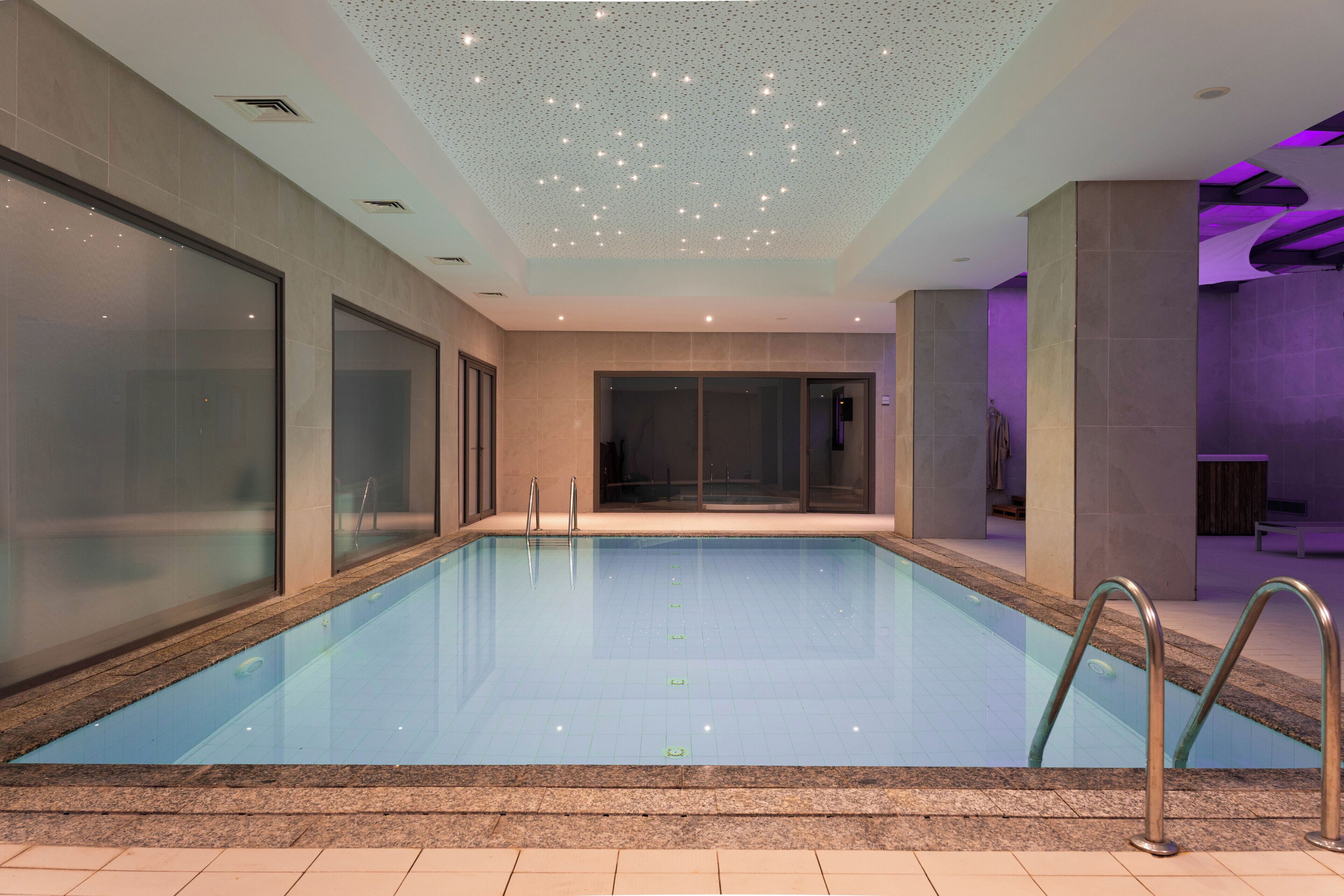 A swimming pool with clear water, surrounded by walls with glass panels and metal railings.