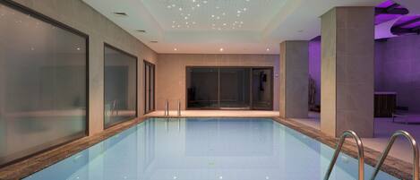 En swimmingpool med klart vand, omgivet af vægge med glaspaneler og metalgelændere.