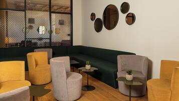 A modern lounge area with sofas, armchairs, and small tables, featuring a large window and decorative wall mirrors.