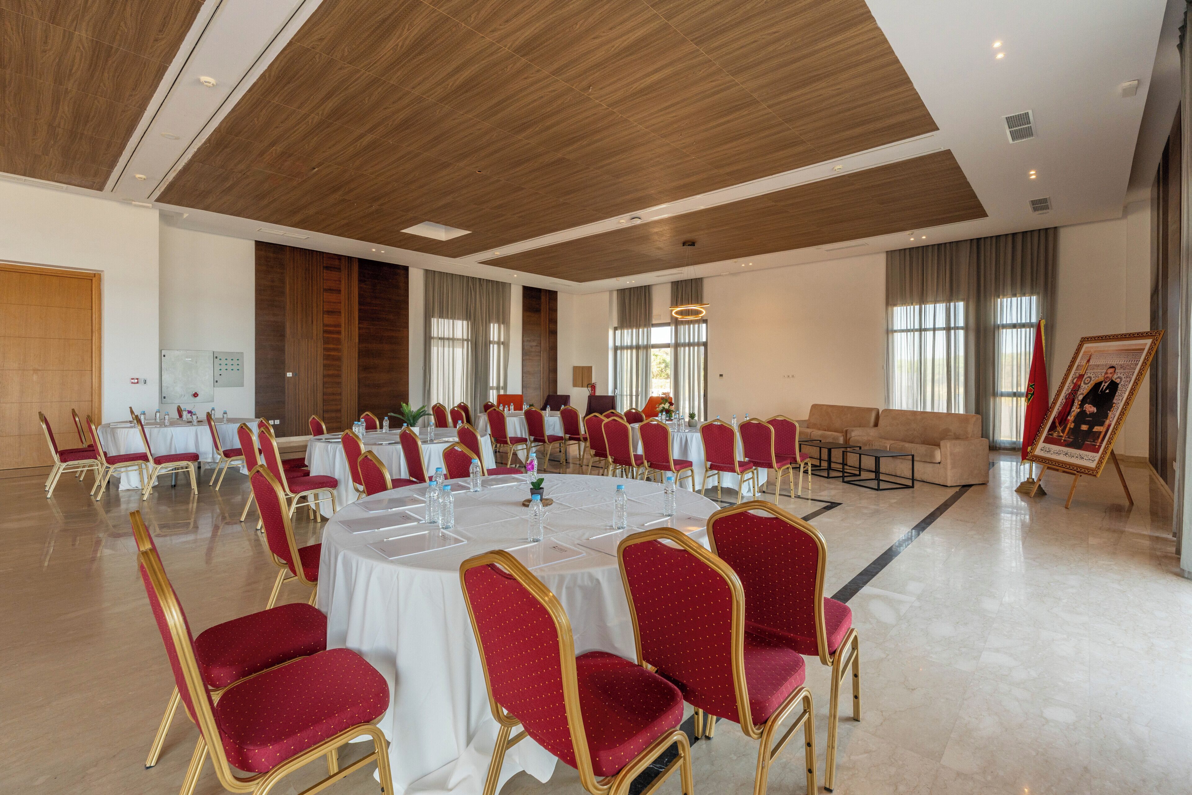 Una sala de conferències amb taules rodones, cadires vermelles i un quadre gran.