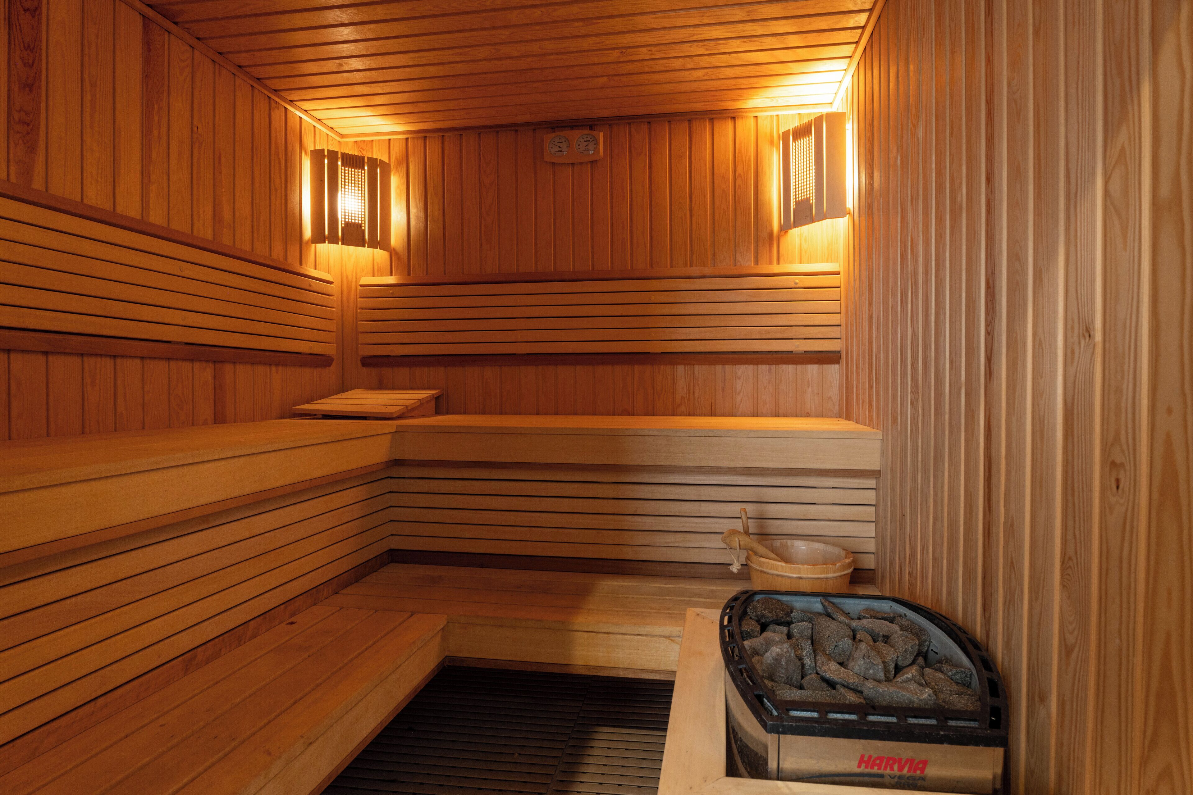 A sauna with wooden benches, a stone basin, and a stone heater labeled 'HARVIA'.