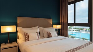 Habitación de hotel con cama, dos lámparas de noche, mesita de noche y ventana con vista a una piscina.
