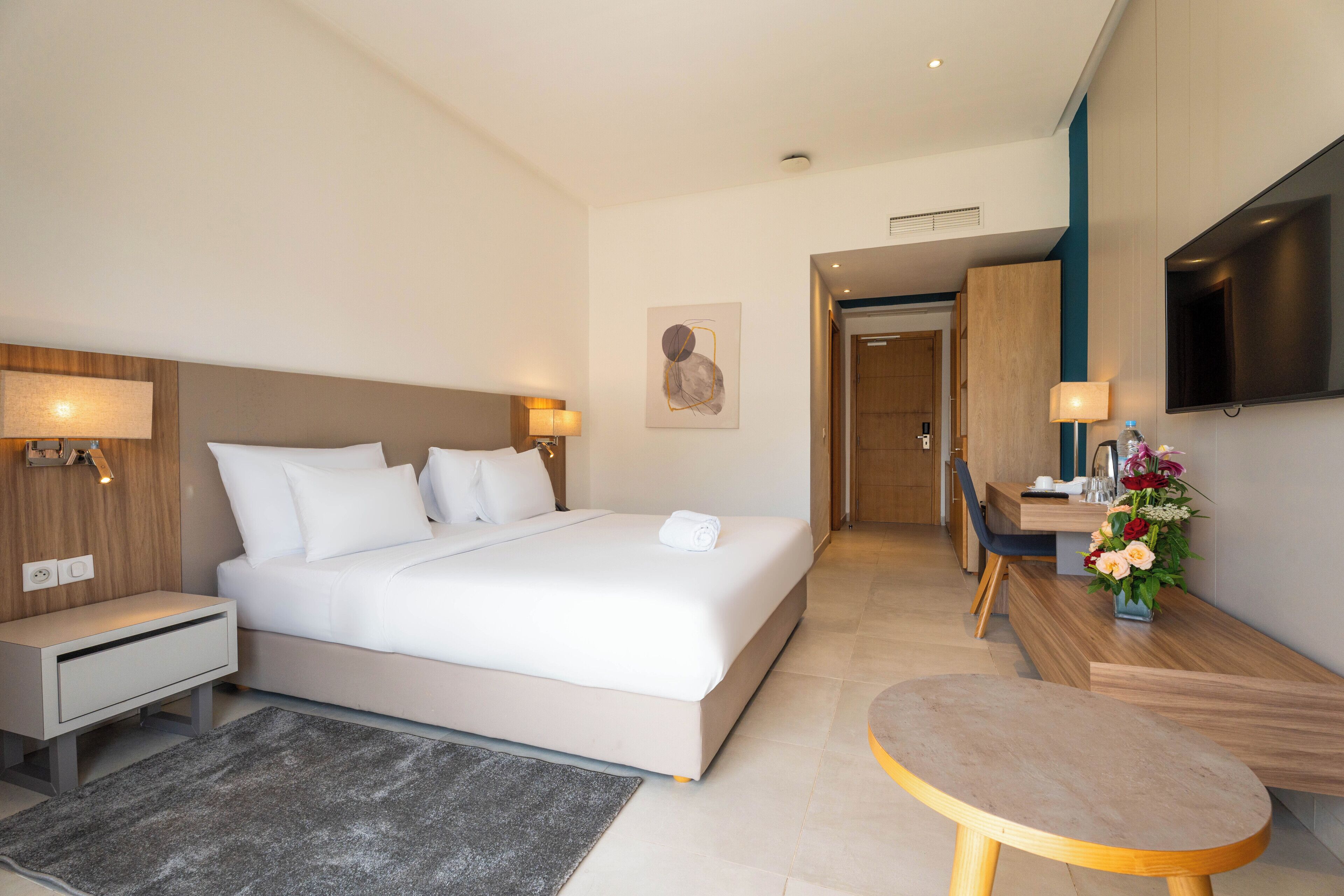 A modern hotel room with a large bed, bedside tables, a desk, and a TV.