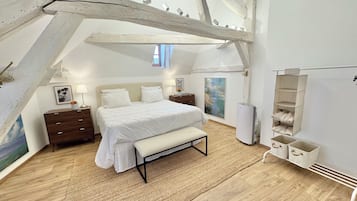 Een slaapkamer met een bed, nachtkastjes, een bankje, een schilderij en een inbouwkast.