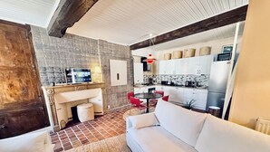 A living room with a sofa, a coffee table, and a TV. There is a kitchen area with white cabinets and a dining table with red chairs. - La Dolce Vita a few steps from everything Beaune has to offer (Beaune)
