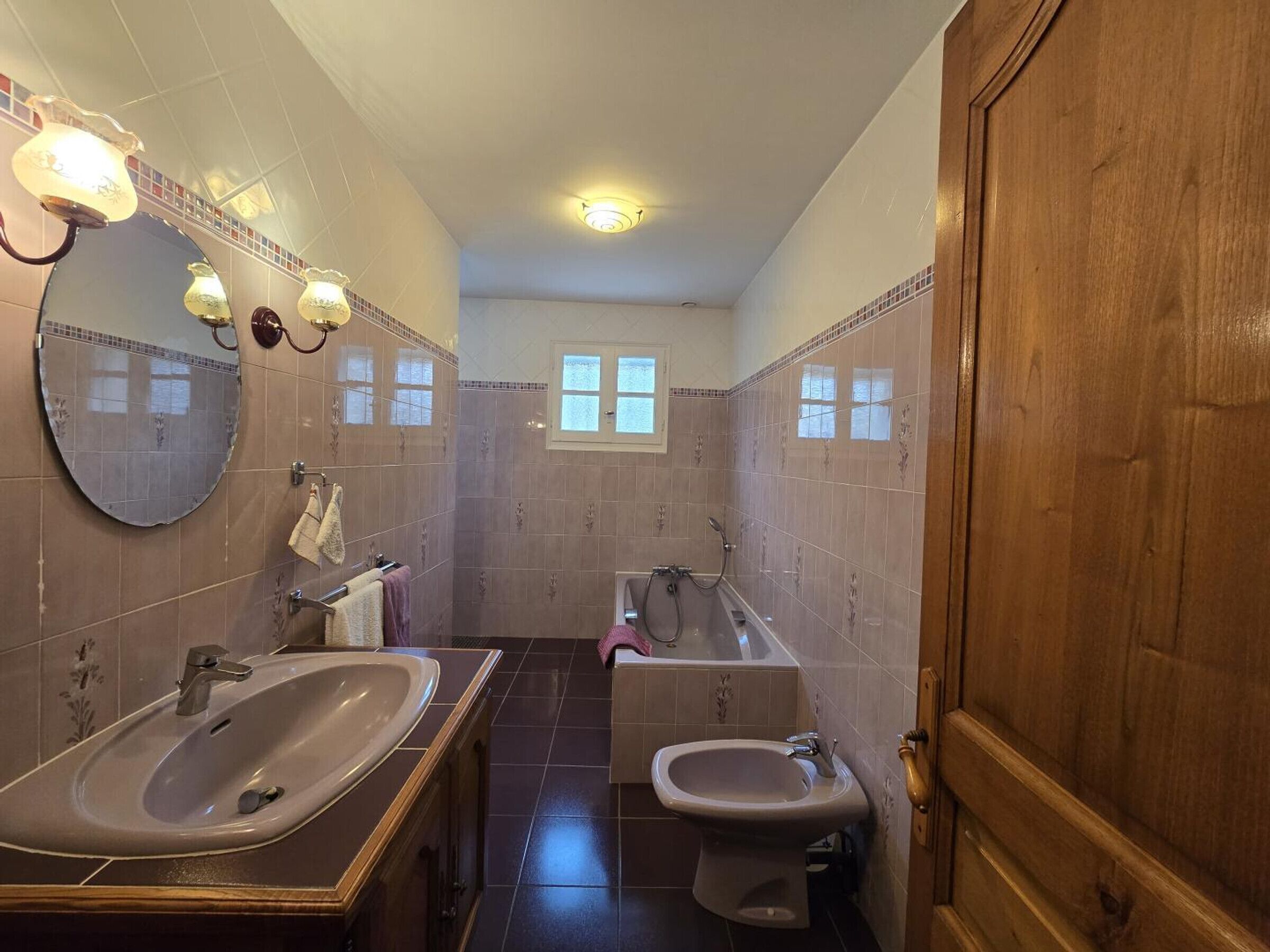 Ein Badezimmer mit zwei Waschbecken, einer Badewanne und einer Dusche. Es gibt Wandleuchten und ein Fenster.