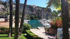 Uma marina com barcos atracados, mar azul cristalino e um penhasco rochoso ao fundo.