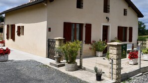 Una casa de dos pisos con fachada color crema, contraventanas rojas y techo de tejas.