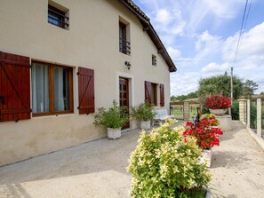 A two-story house with a beige exterior, wooden shutters, and a small porch area with potted plants and a bench. - Charming home for 6 in Dordogne, nature retreat (Saint-Michel-de-Double)