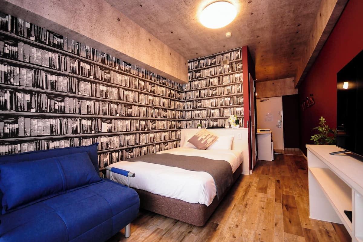 Un dormitorio con una amplia estantería, una cama, un sofá azul y un televisor.