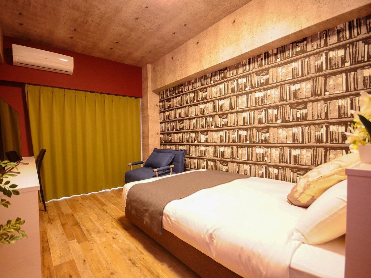 A bedroom with a large bed, a desk, a chair, and a bookshelf wall.