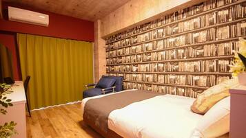 A bedroom with a large bed, a desk, a chair, and a bookshelf wall.