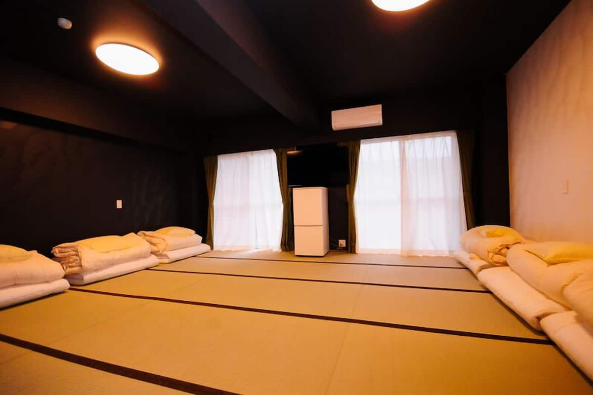 Una habitación con esteras de tatami, un futón, un calentador y una ventana con cortinas.