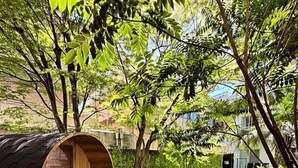 Una estructura de barril de madera con un banco en su interior, rodeada de hierba verde exuberante y árboles.