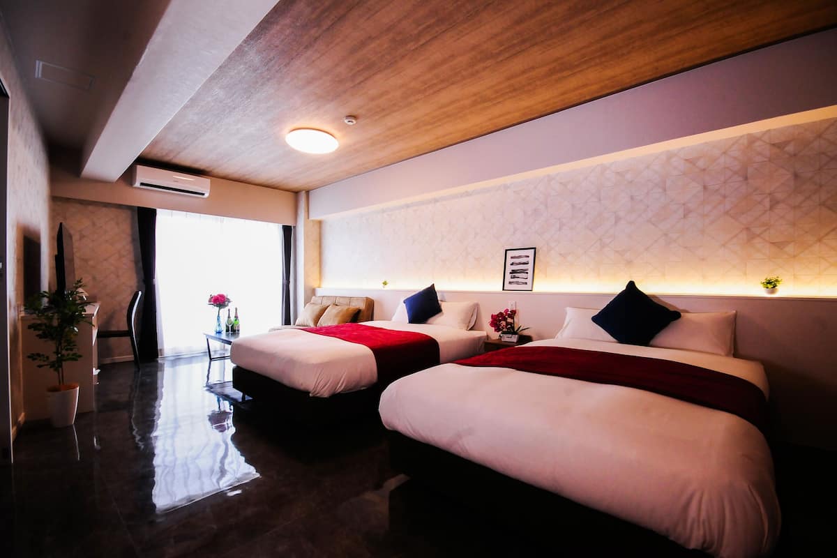 Habitación de hotel con dos camas, techo de madera, aire acondicionado montado en la pared, una mesita con un florero y un ventanal grande.