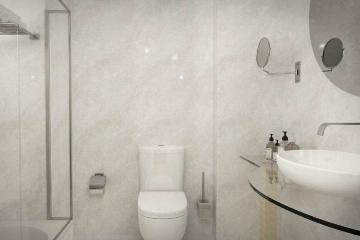 A modern bathroom with a glass shower enclosure, a white toilet, a round sink, and a wall-mounted mirror.