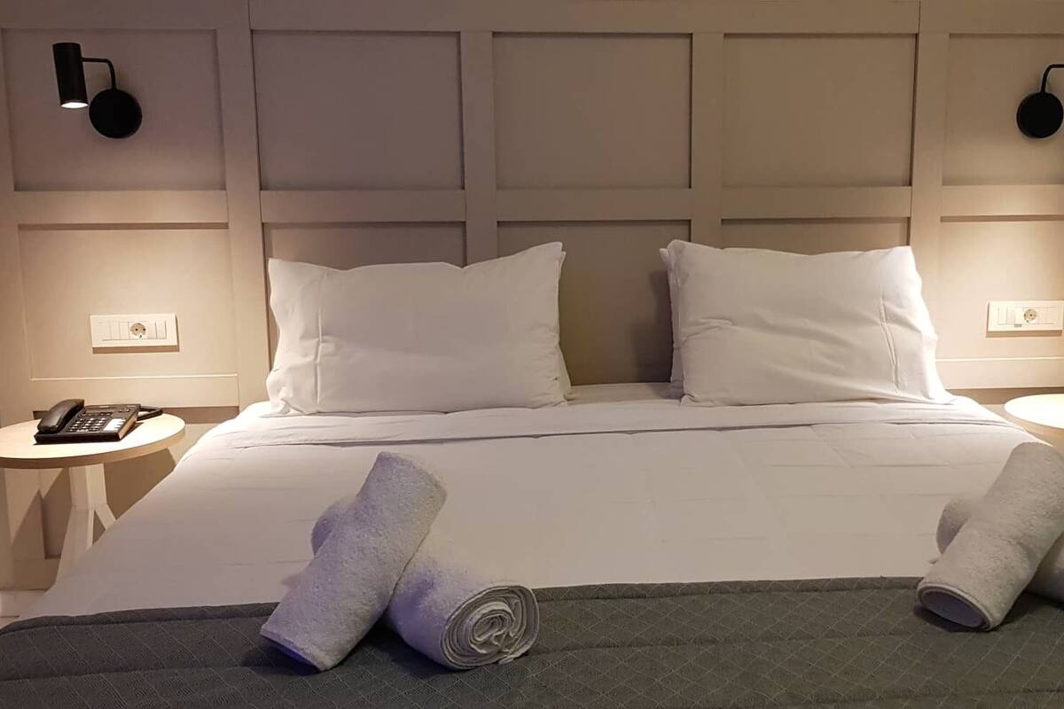 A neatly made bed with white linens and pillows, two bedside tables with lamps, and a telephone on one of the tables.