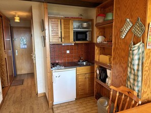 A compact kitchen with wooden cabinets, a microwave, a sink, and a small refrigerator.