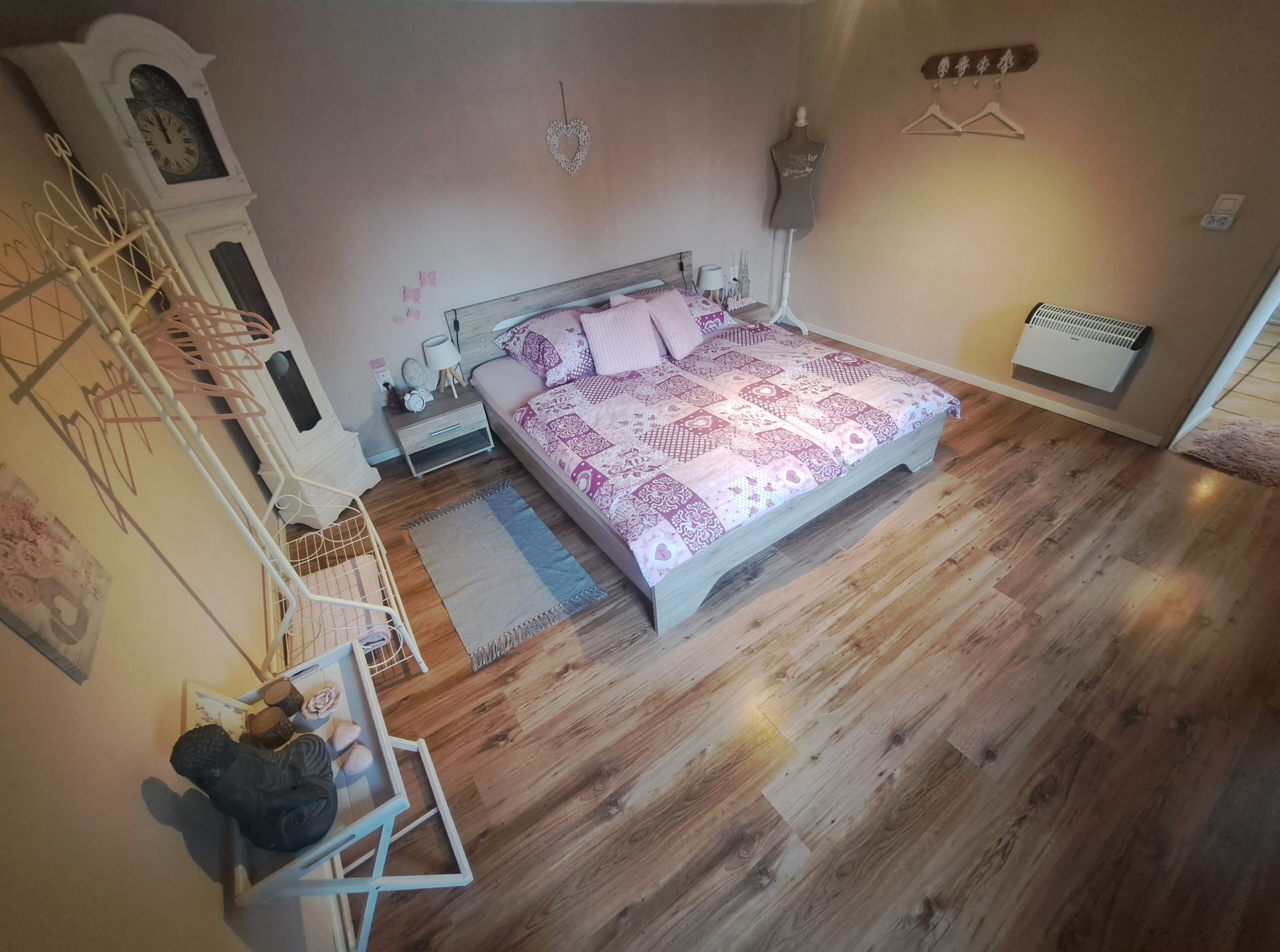 Une chambre avec un plancher en bois, un lit avec une literie à motifs, une commode, une horloge et un radiateur fixé au mur.
