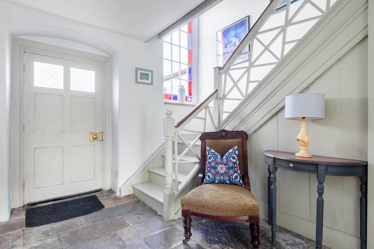 A staircase with white balusters, a wooden chair with a patterned cushion, and a small table with a lamp.