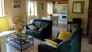 A cozy living room with a black leather sofa, a green sofa, and a coffee table with a vase of flowers. There is a dining area with a table and chairs, and a kitchen in the background. - Charming Perigord house in Salignac-Eyvigues, pets allowed (Salignac-Eyvigues)
