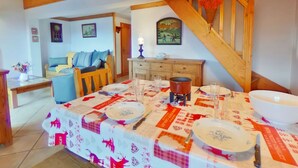 A dining area with a wooden table set for a meal, a sofa in the background, and a staircase with a wooden railing. - 4-Room Mezzanine Apt Les Saisies 10 guests (Villard-sur-Doron)