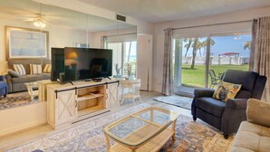 A living room with a TV, sofa, and armchair, large windows with a view of the beach, and a ceiling fan. - El Matador 417 - FREE TICKETS!! Your stay includes free tickets to many area attractions! (Fort Walton Beach)