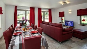 A dining area with a long table set for four, red upholstered chairs, a sofa, and a television. - Spacious house with private pool and pets allowed (Cénac-et-Saint-Julien)