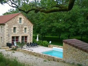 Un bâtiment en pierre avec un toit rouge, une piscine et un espace extérieur aménagé pour s’asseoir.