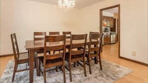 Ein Esszimmer mit Holztisch und -stühlen, einer Kristallleuchter und Blick in die Küche.