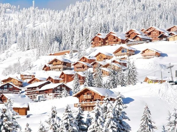 Een besneeuwd bergdoordal met houten chalets, omringd door sneeuwbedekte bomen en een heldere lucht.