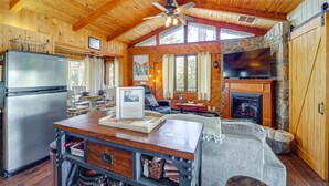 A rustic cabin interior with a wooden ceiling, a stone fireplace, a television, and a dining area. - Near Lake + Trails: Rustic Newland Cabin w/ Deck! (Newland)