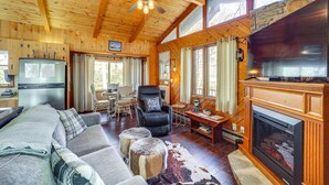 A cozy cabin interior with a wooden ceiling, a fireplace, a sofa, a dining area, and a kitchen with a refrigerator. - Near Lake + Trails: Rustic Newland Cabin w/ Deck! (Newland)