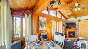 A cozy cabin interior with a wooden interior, a fireplace, and a dining area with a table set for four. - Near Lake + Trails: Rustic Newland Cabin w/ Deck! (Newland)