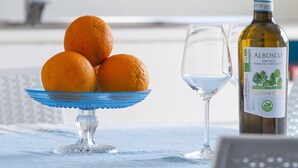 Een keuken met een blauwe kom mandarijnen, een wijnfles en een glas op een tafel.