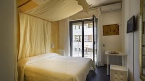 Een hotelkamer met een bed, een tafeltje, een bankje, een televisie en een balkon met uitzicht.