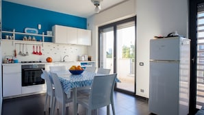 Een moderne keuken met witte kasten, een blauwe wand en een eethoek met een tafel en stoelen.