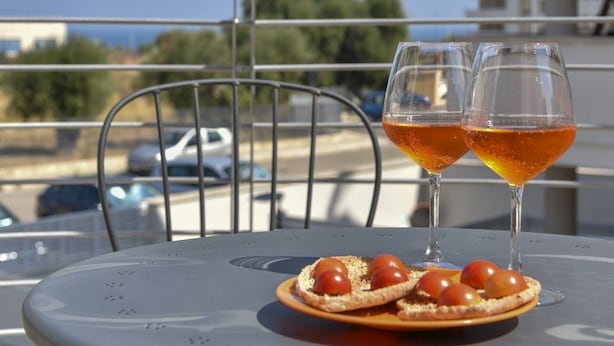 Een tafel met twee glazen oranje vloeistof, een bord met kerstomaatjes en een metalen stoel op een balkon.