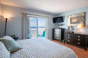 A bedroom with a bed, a dresser, a TV, and a balcony with a chair. - Ocean Dunes 2005 Wait N Sea (Kure Beach)