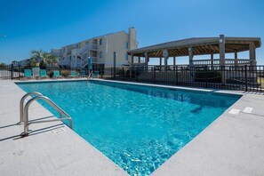 A swimming pool with a metal ladder, a covered seating area, and a building with balconies in the background. - Ocean Dunes 2005 Wait N Sea (Kure Beach)