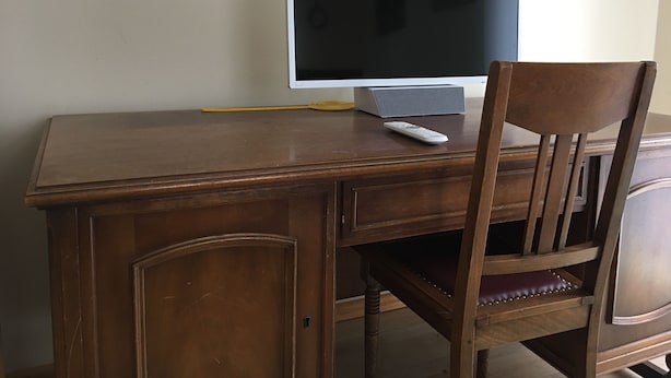 A wooden desk with a flat-screen TV, a remote control, and a pencil.